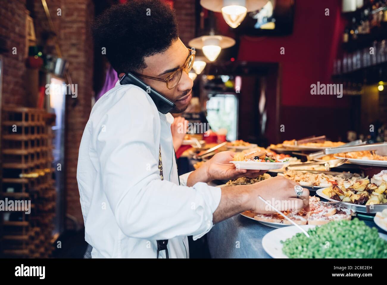 Ein junger Mann am Telefon nahm das Essen vom Buffet Ein Restaurant Stockfoto