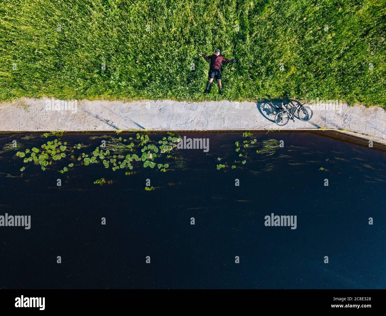 Drohnenaufnahme eines mittelerwachsenen Mannes mit Fahrrad liegend Grasland an der Flussküste Stockfoto