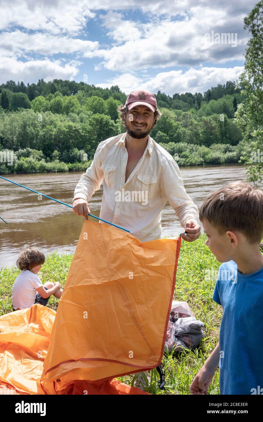 Vater mit Söhnen Installation Zelt auf dem Campingplatz gegen See in Wald Stockfoto