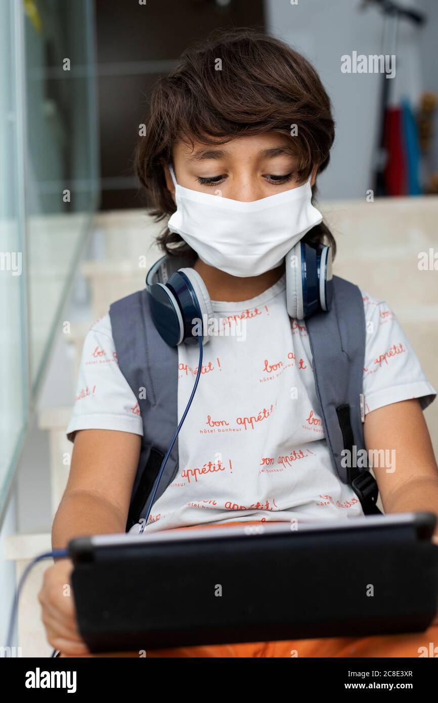 Nahaufnahme des Jungen trägt Gesichtsmaske mit digitalen Tablet, während Sitzen auf Stufen in der Schule Stockfoto