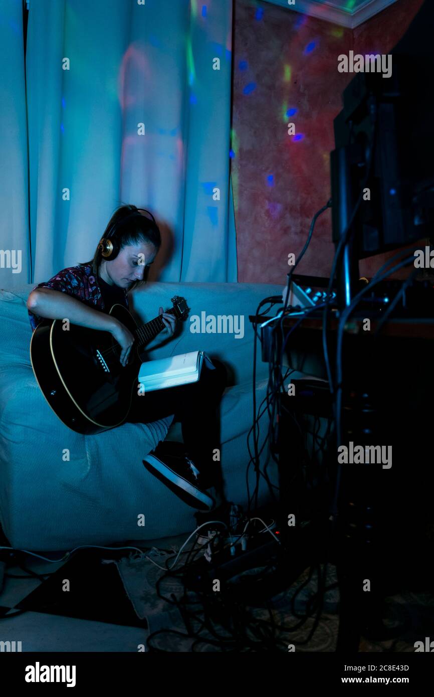 Musikerin liest Buch beim Spielen Gitarre auf Sofa in Aufnahmestudio zu Hause Stockfoto