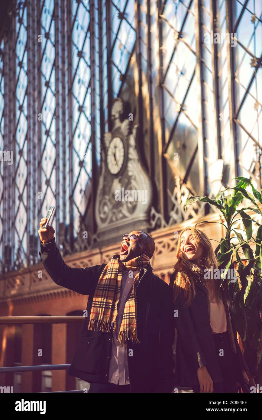 Fröhlicher Geschäftsmann, der Selfie mit einer Kollegin nimmt, während er dabei steht Station Stockfoto