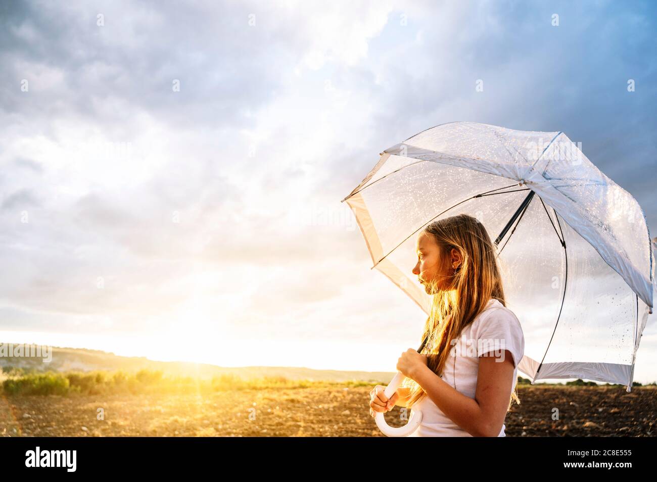 Mädchen hält Regenschirm während Blick weg während Sonnenuntergang Stockfoto
