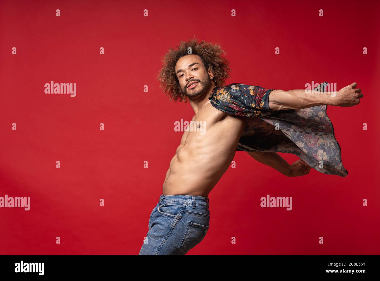 Junger Mann in einem vollständig unknöpfbaren Hemd, der vor rotem Hintergrund tanzt Stockfoto