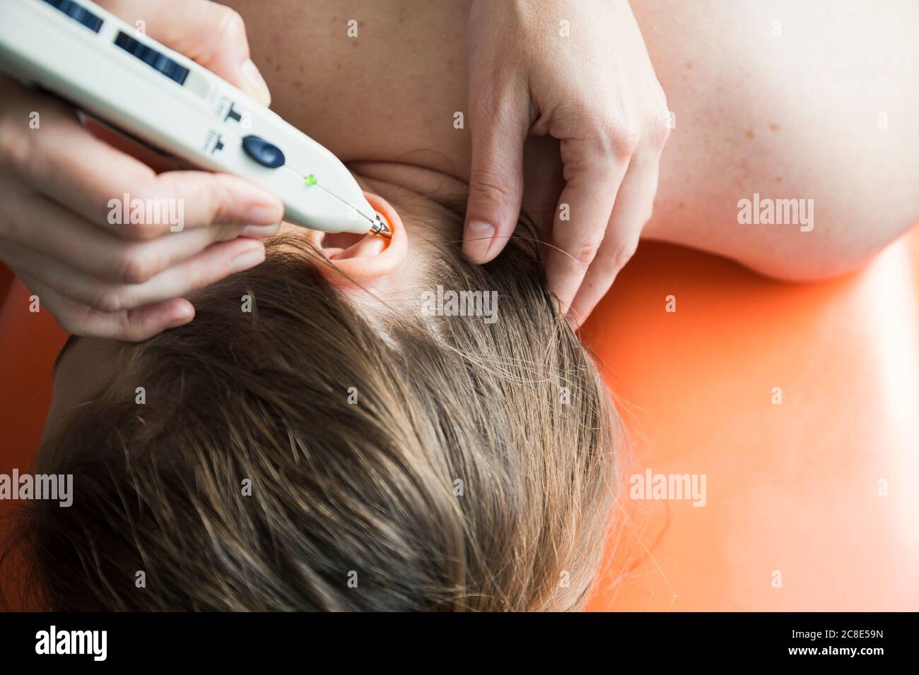 Physiotherapeut mit Stimulator der Akupunkturpunkte auf dem Ohr der Frau Patient Stockfoto