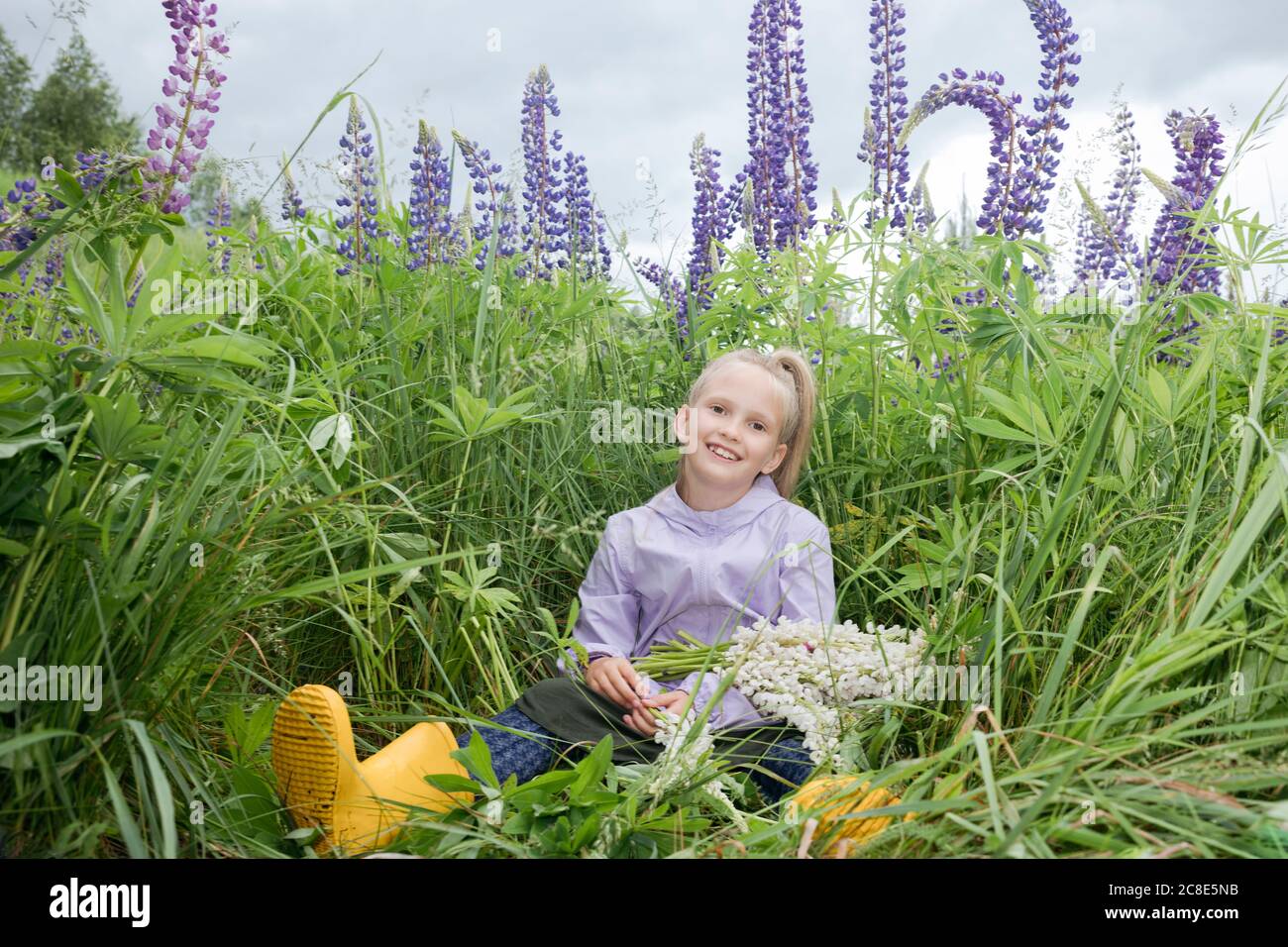 Portrait von glücklichen Mädchen vor Lupine Feld sitzen Mit Blumenstrauß gepflückt Stockfoto