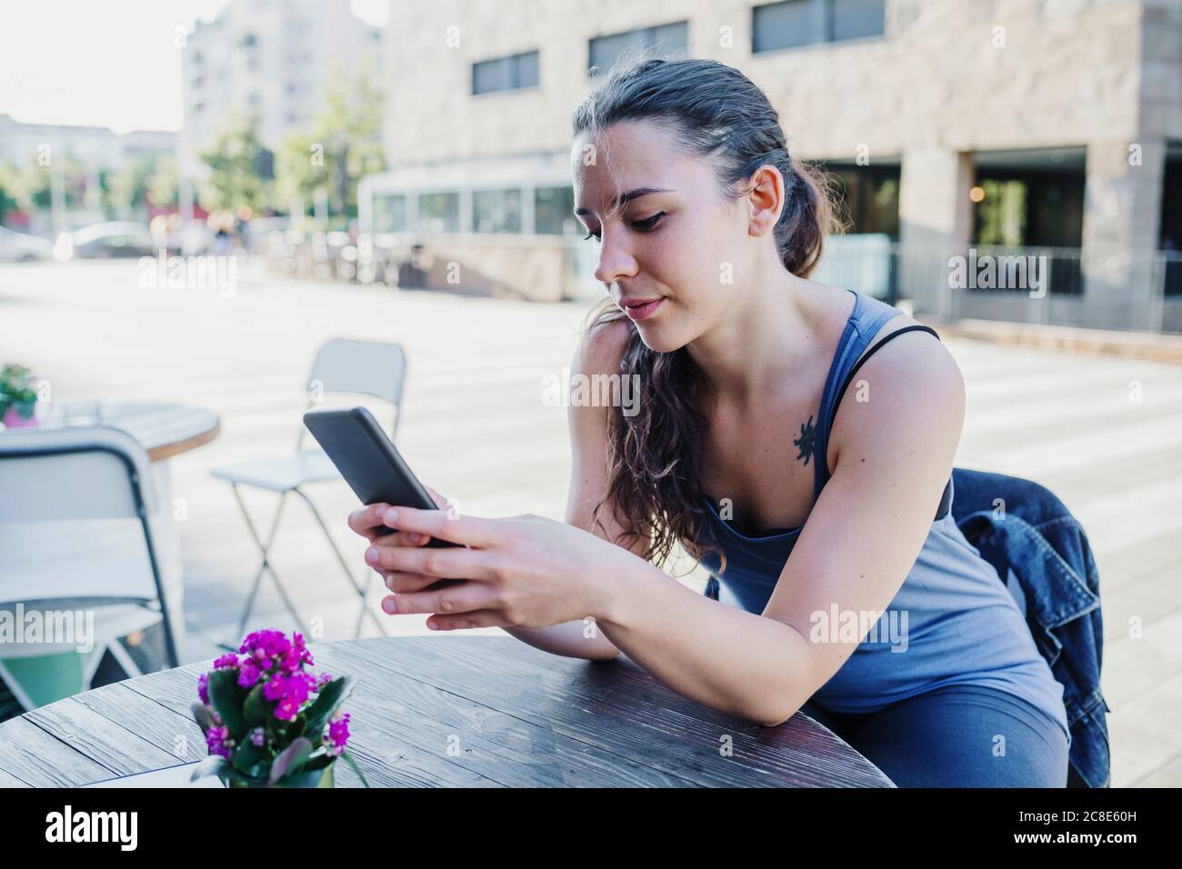 Sportliche junge Frau mit Smartphone, während sie auf dem Bürgersteig sitzt Café Stockfoto