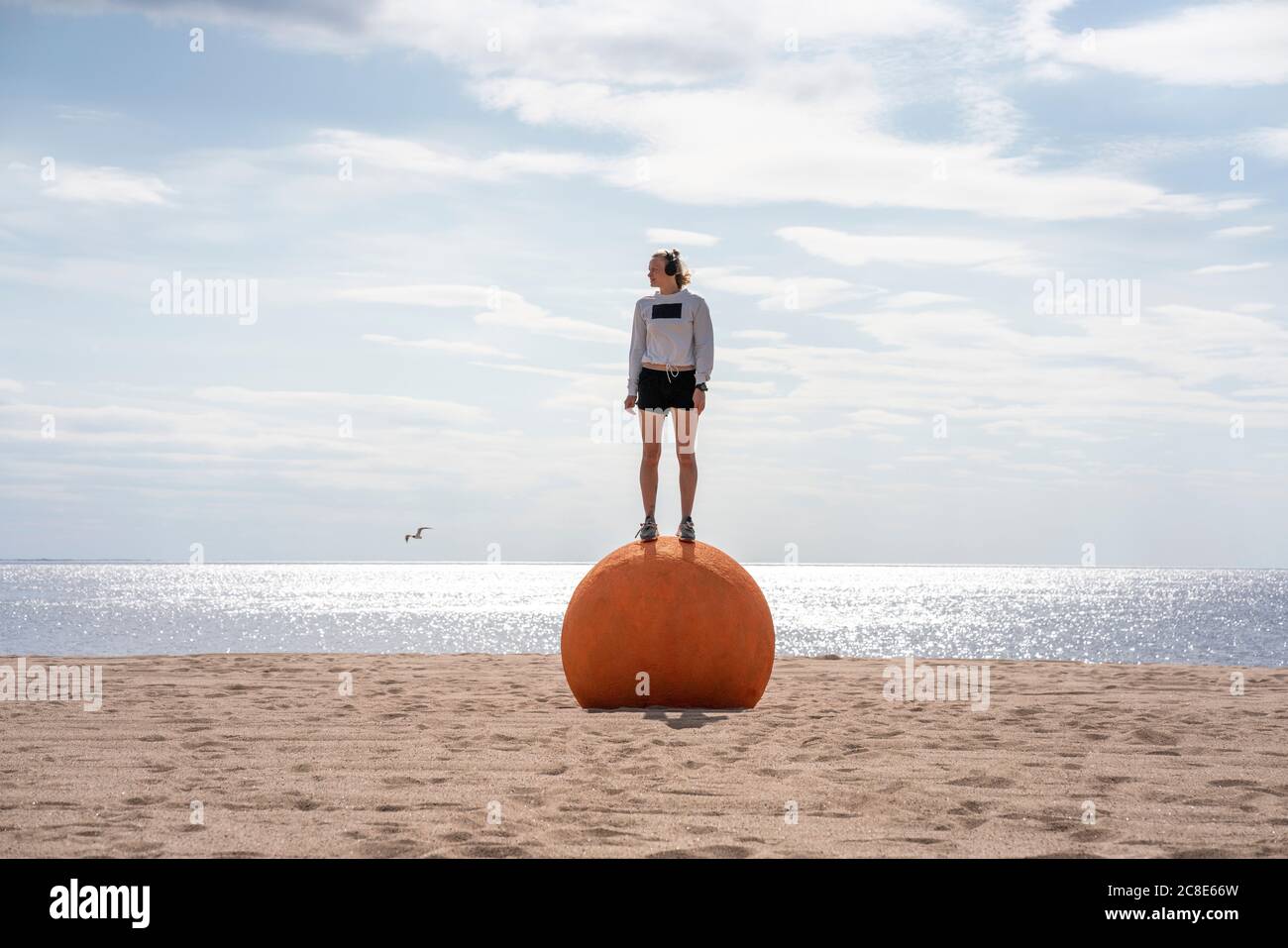 Junge Frau, die am Strand auf orangefarbenem Stein steht Stockfoto