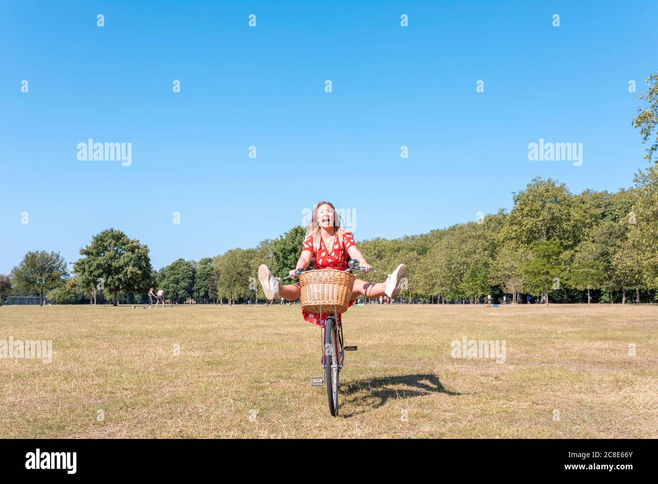 Fröhliche Frau mit den Füßen auf Fahrrad auf dem Feld gegen Blauer Himmel Stockfoto