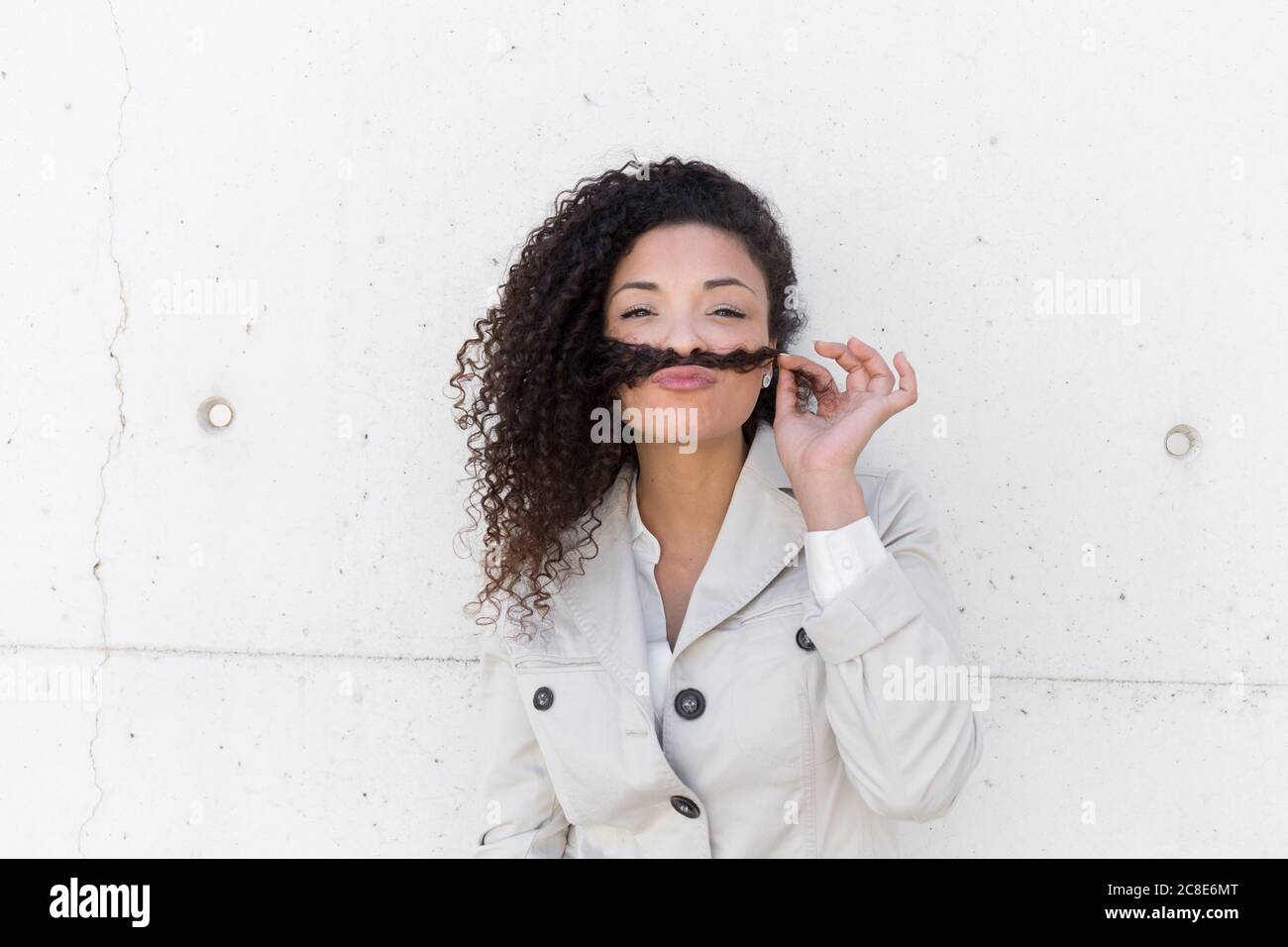 Stilvolle Geschäftsfrau hält Haare auf den Lippen wie Schnurrbart an der Wand Stockfoto