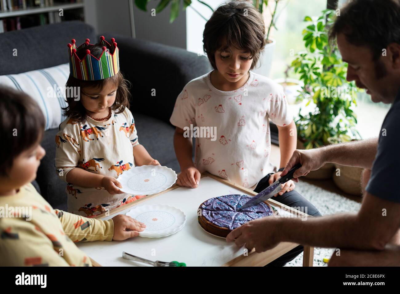 Vater schneiden Geburtstagskuchen für seine drei Kinder in der Wohnzimmer Stockfoto