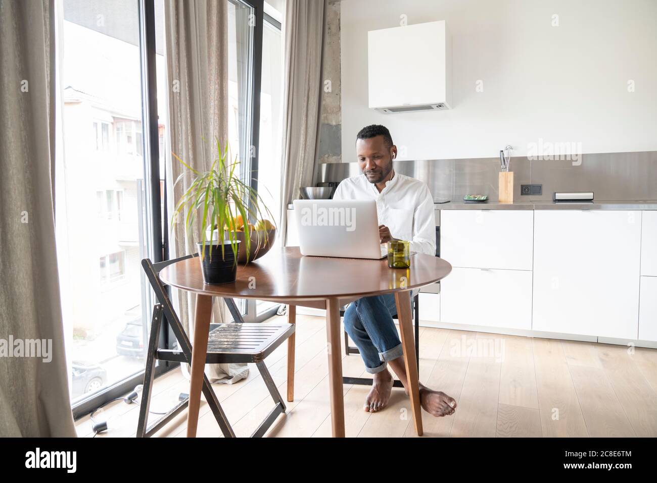 Portrait des Mannes am Tisch sitzen in modernen Wohnung mit Laptop und Kopfhörer Stockfoto
