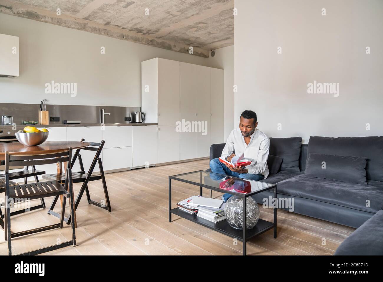 Mann sitzt auf der Couch in der modernen Wohnung Umblättern in Ein Buch Stockfoto