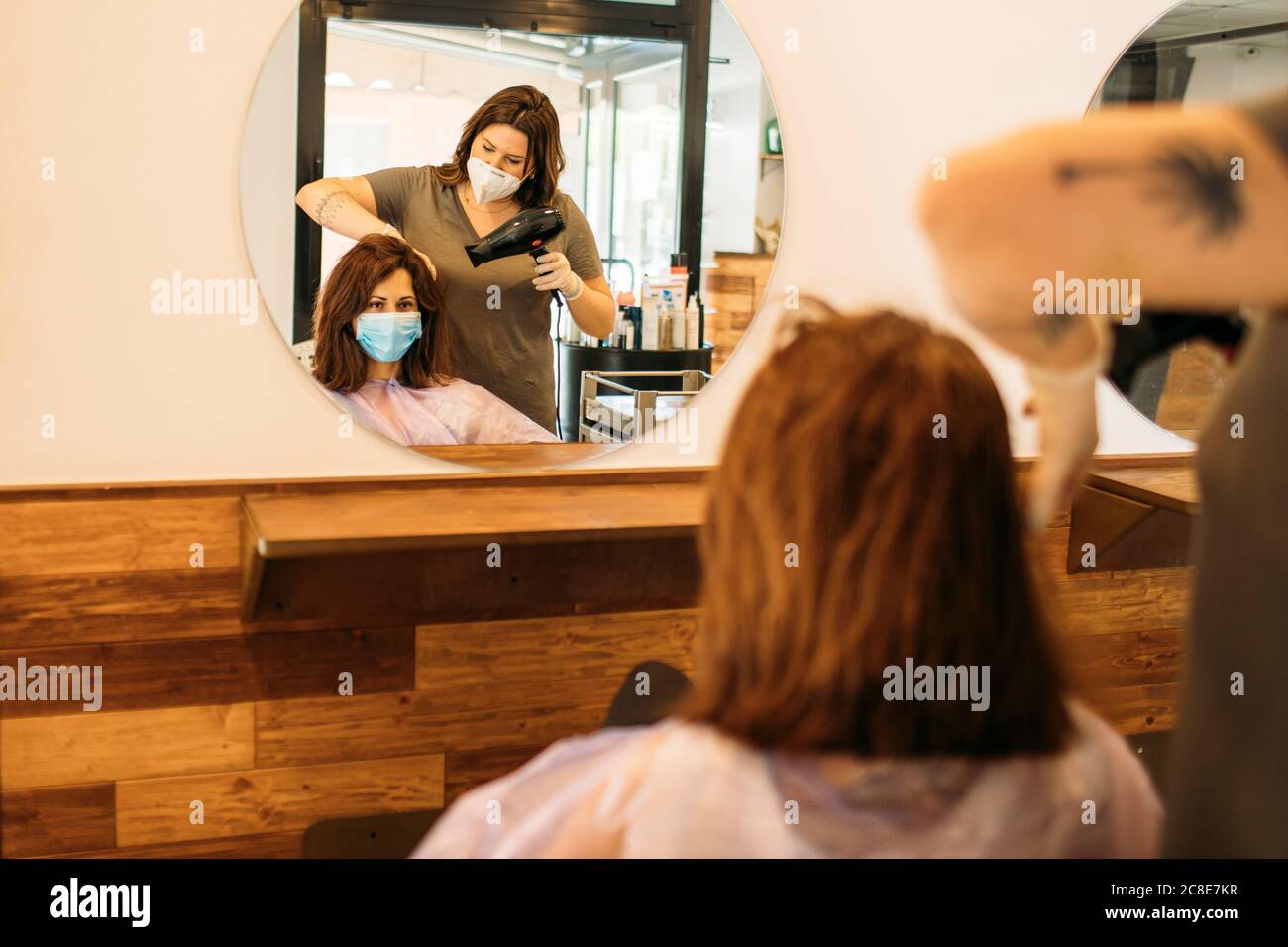 Weibliche Friseur trocknet Haar der weiblichen Kunden mit Maske Stockfoto