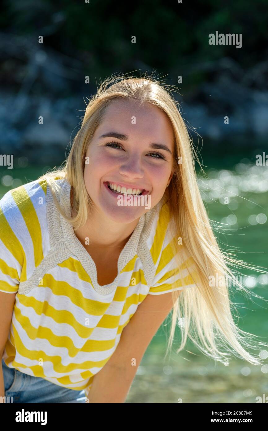 Lächelnde junge Frau mit blonden Haaren, die gegen den Fluss stehen Stockfoto