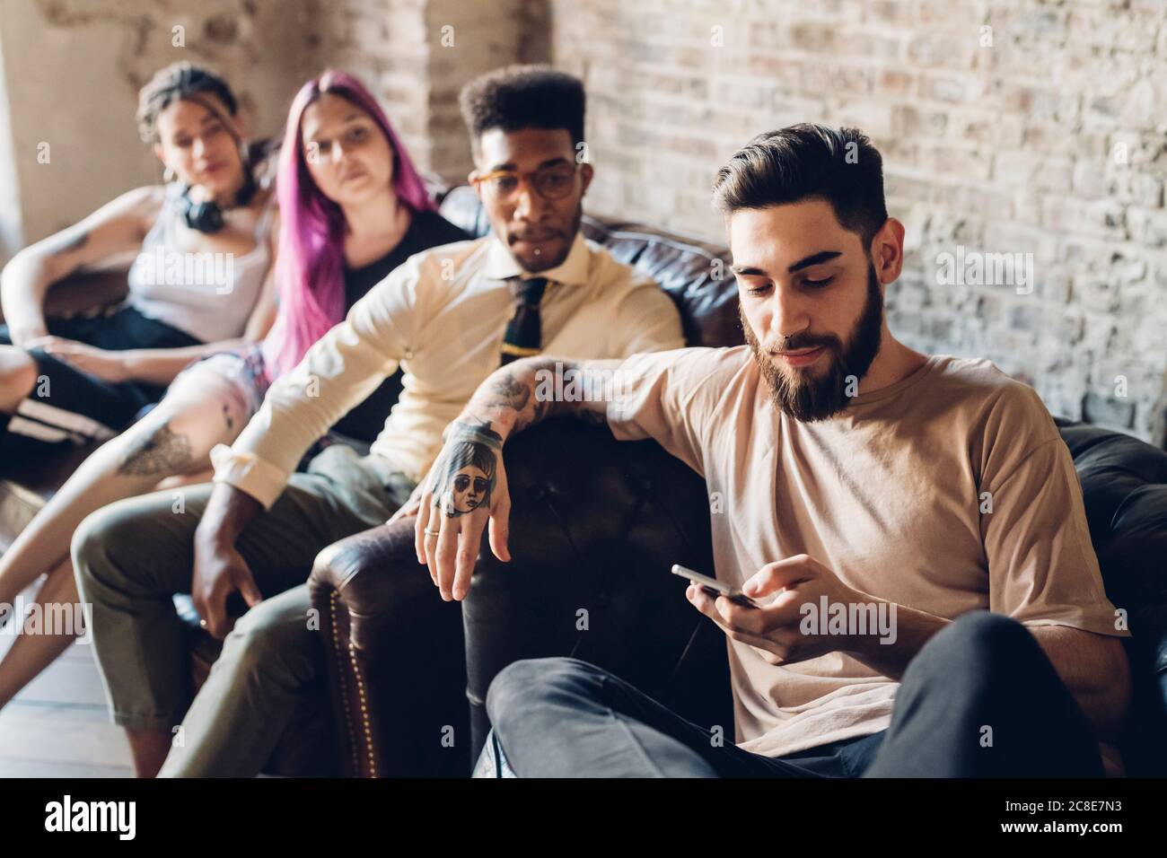 Gruppe von Freunden sitzen auf dem Sofa in einem Loft mit Smartphone Stockfoto