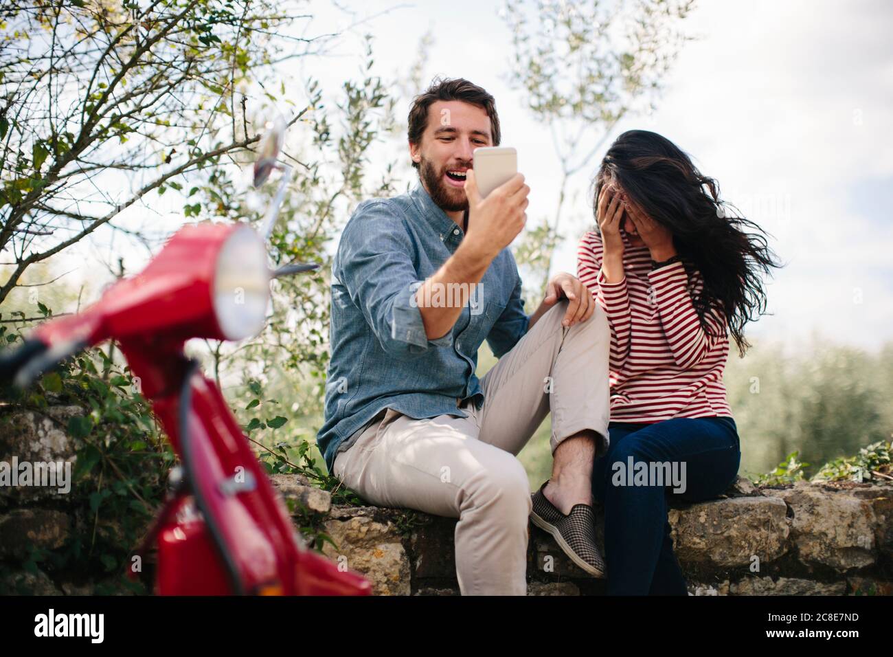 Glücklicher Mann mit Smartphone, während er mit Freundin auf sitzt Haltewand Stockfoto