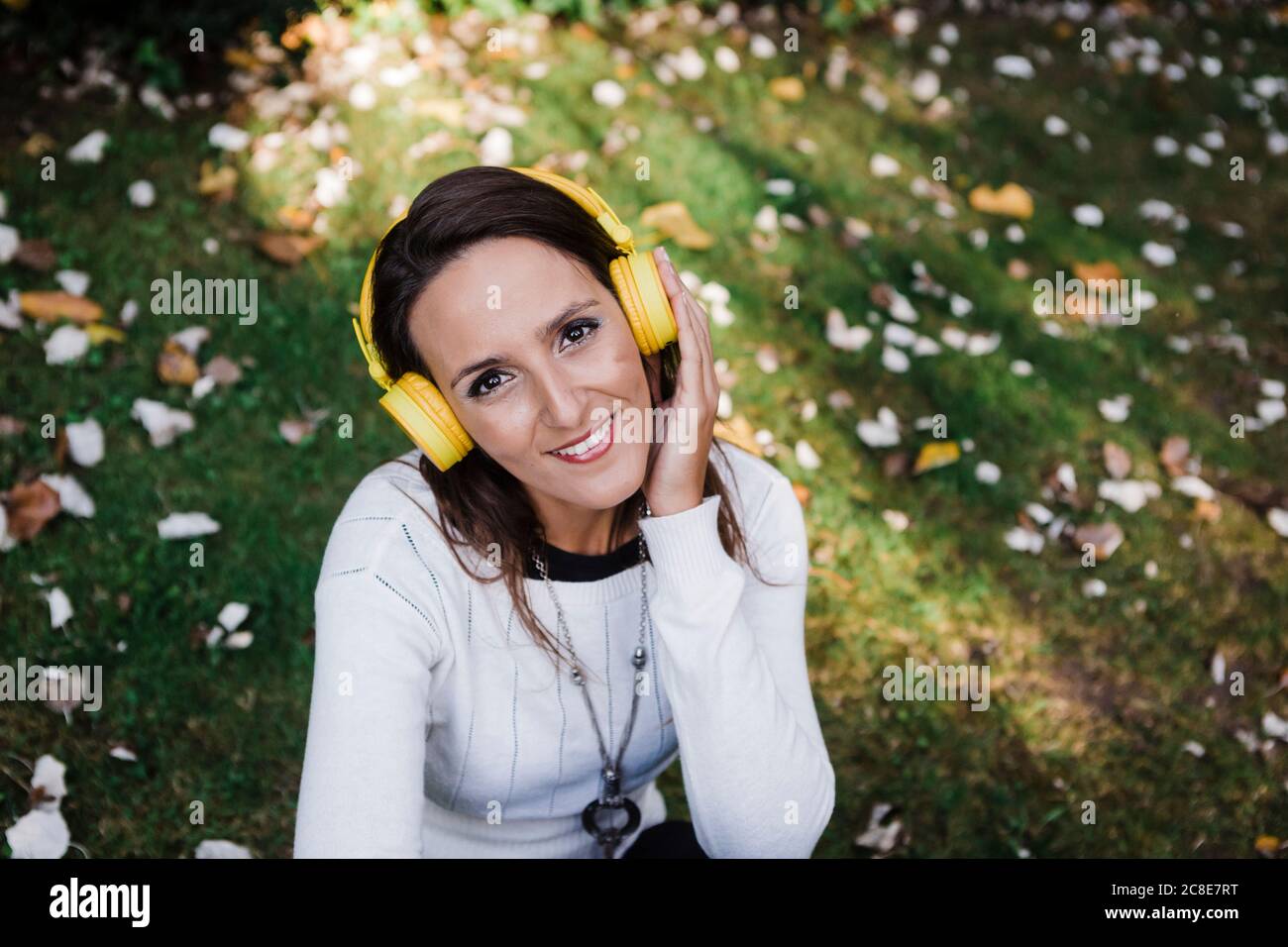 Glückliche, schöne Frau, die Musik hört, während sie im Park sitzt Stockfoto