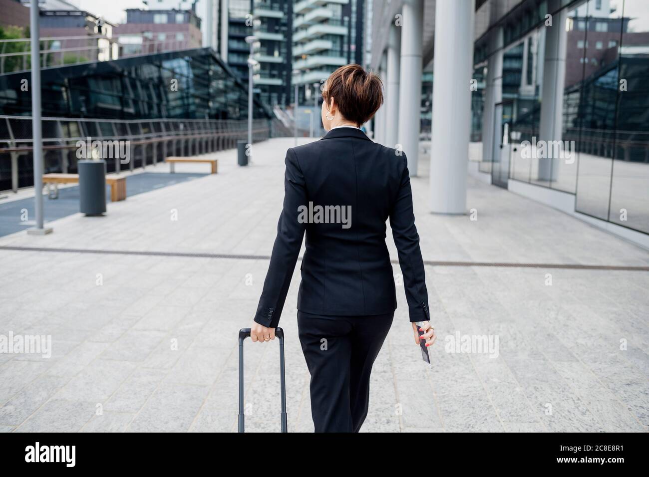 Geschäftsfrau mit kurzen Haaren hält Koffer beim Gehen mit Fußpfad In der Stadt Stockfoto