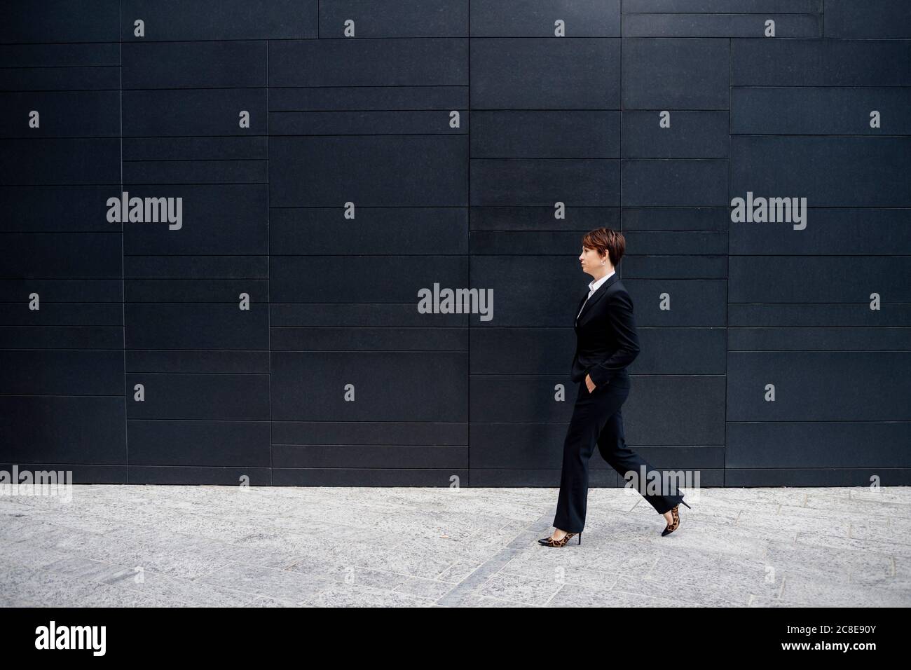 Geschäftsfrau mit kurzen Haaren, die auf dem Bürgersteig durch ein modernes Gebäude läuft In der Stadt Stockfoto