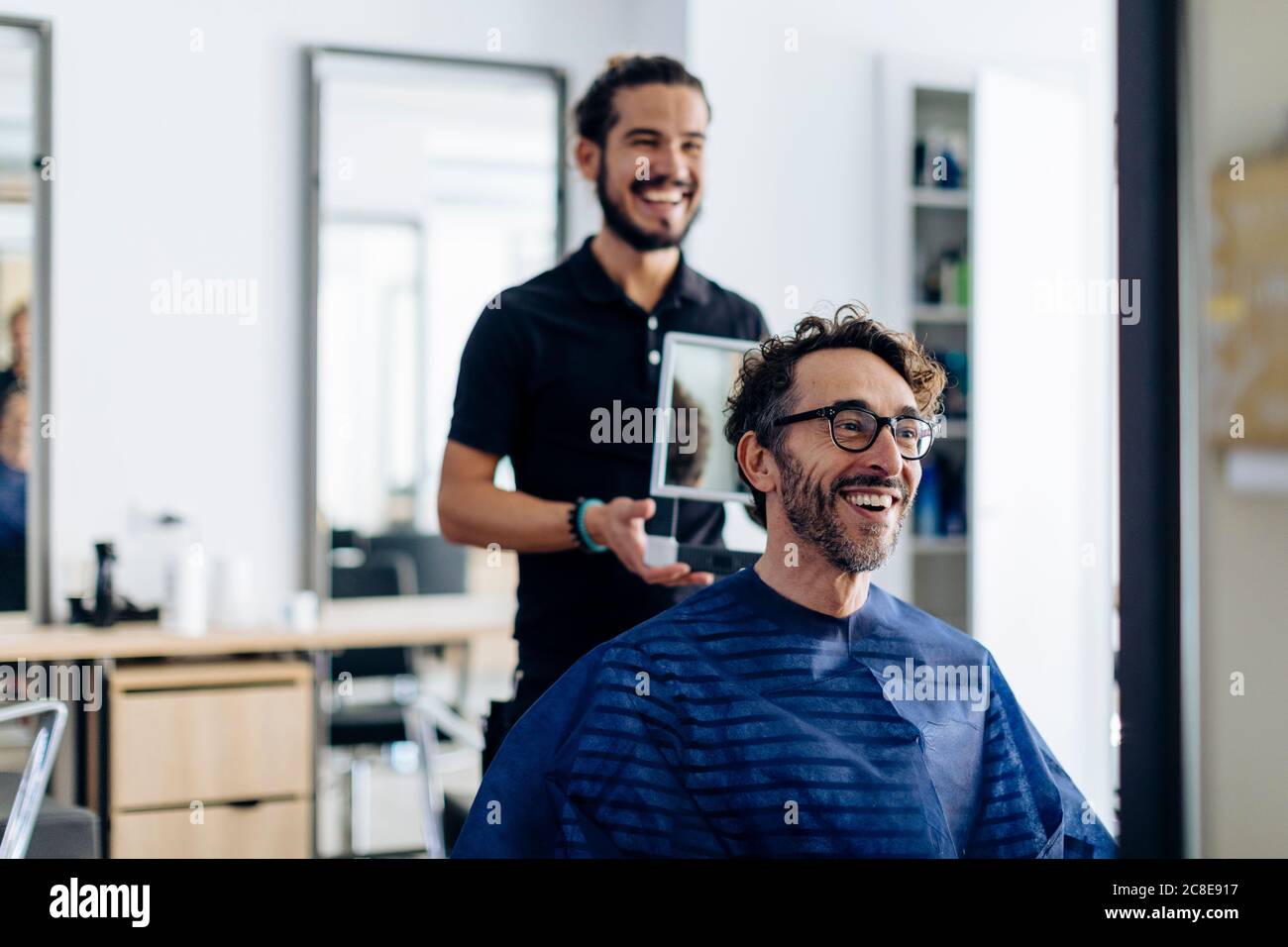 Ein glücklicher Friseur zeigte dem Kunden im Spiegel im Salon einen Haarschnitt Stockfoto