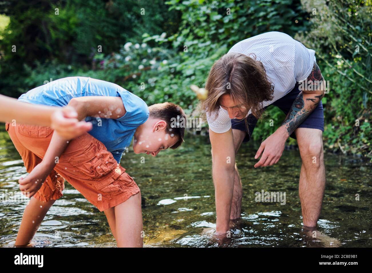 Mann, der mit dem Jungen im Bachwasser am Wald erkundet Stockfoto