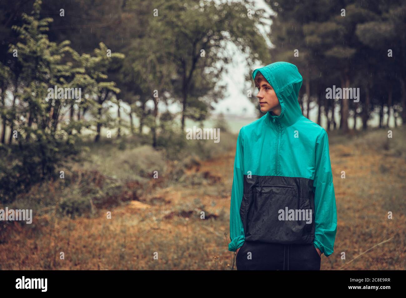 Teenager trägt Regenmantel im Wald, Blick seitlich Stockfoto