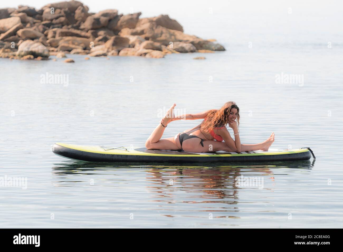 Lächelnde flexible Frau, die Yoga auf dem Paddleboard praktiziert Stockfoto