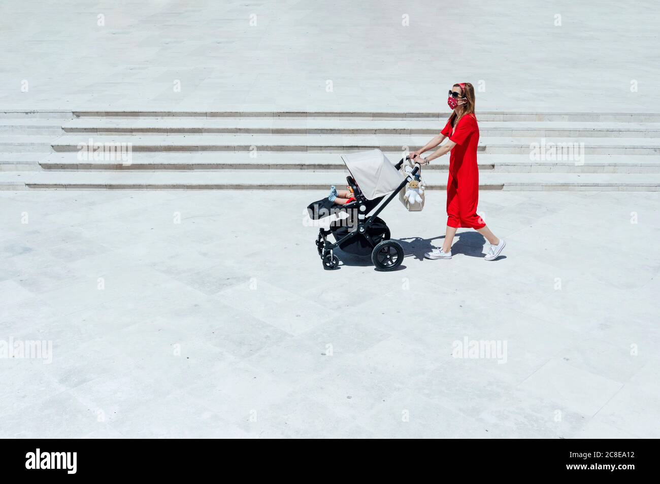 Mutter trägt Maske schieben Sohn in Baby-Wagen beim Gehen Auf dem Marktplatz Stockfoto