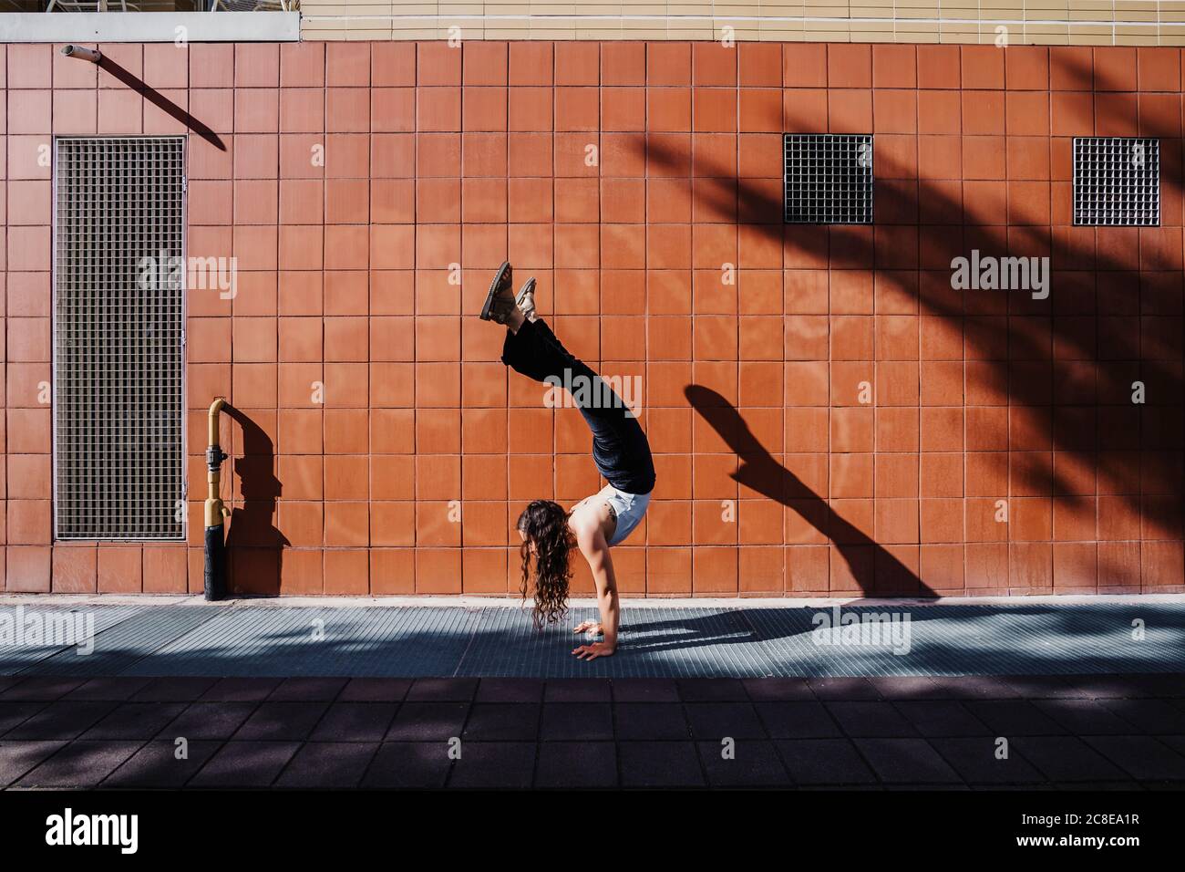 Junge Frau, die Handstand auf dem Bürgersteig gegen geflieste Wand in Stadt Stockfoto