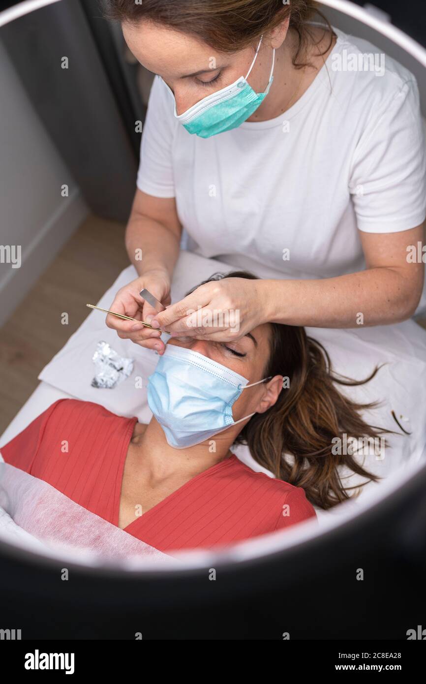 Reife weibliche Kosmetikerin mit Handwerkzeugen für Wimpernverlängerung auf Kunde Stockfoto