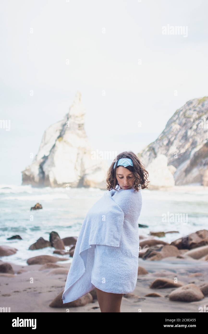 Junge Frau in Handtuch gewickelt, während sie am Strand von Ursa, Portugal, stand Stockfoto