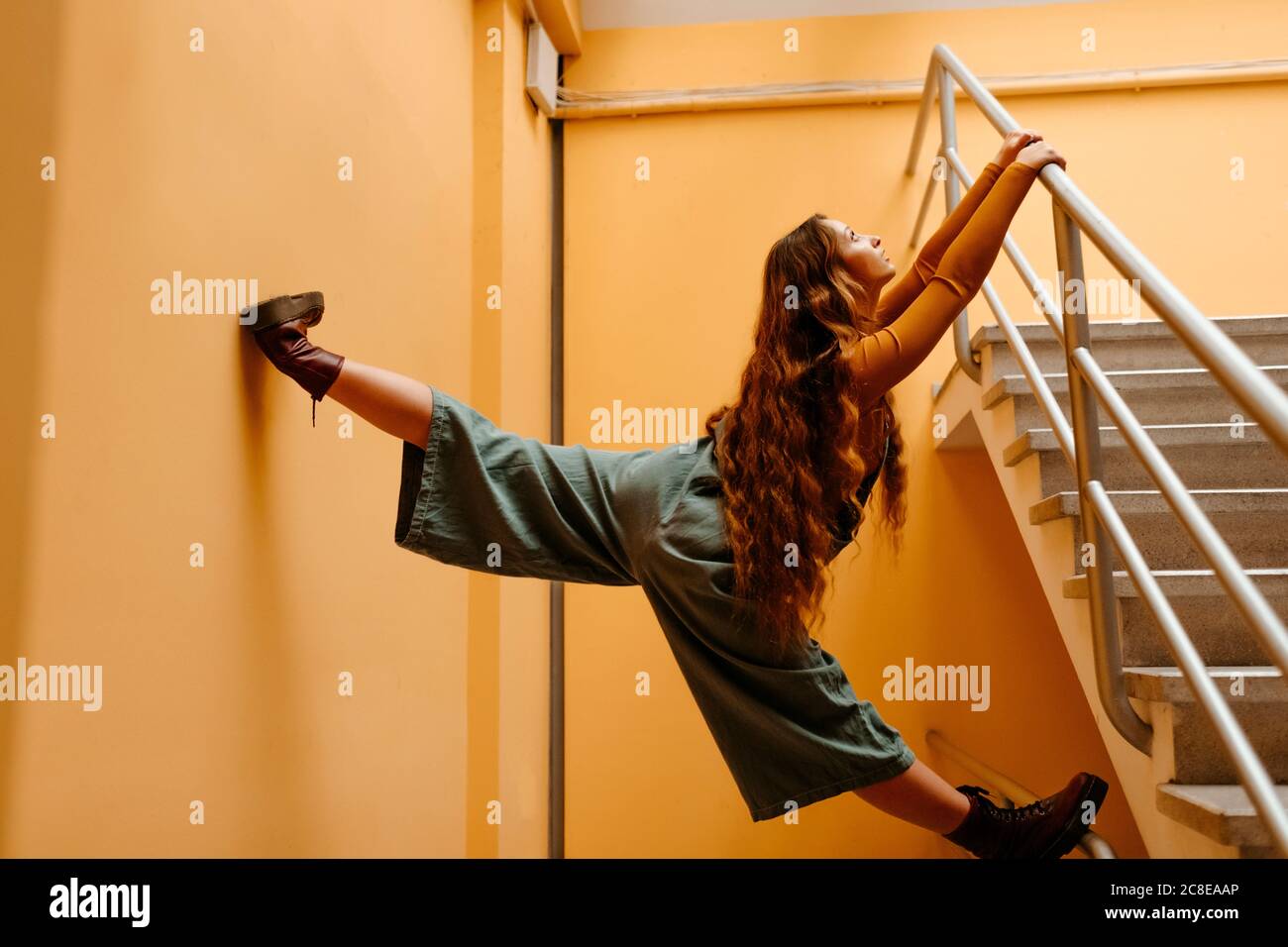 Junge Frau in Jumpsuit auf Geländer vor stehen Orangefarbene Wand Stockfoto