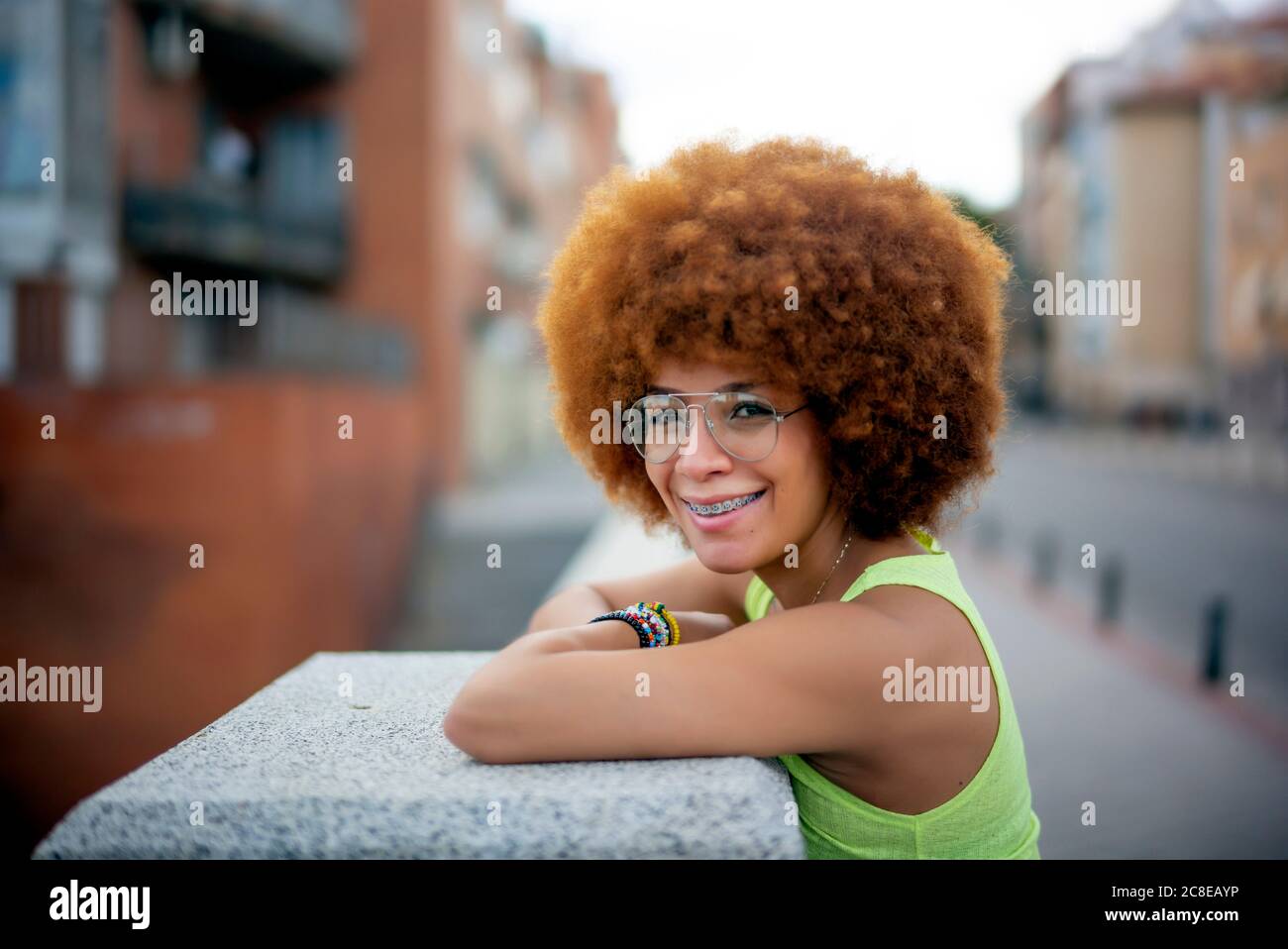 Nahaufnahme der lächelnden Frau mit afro Haar stehend durch Halten Mauer in der Stadt Stockfoto