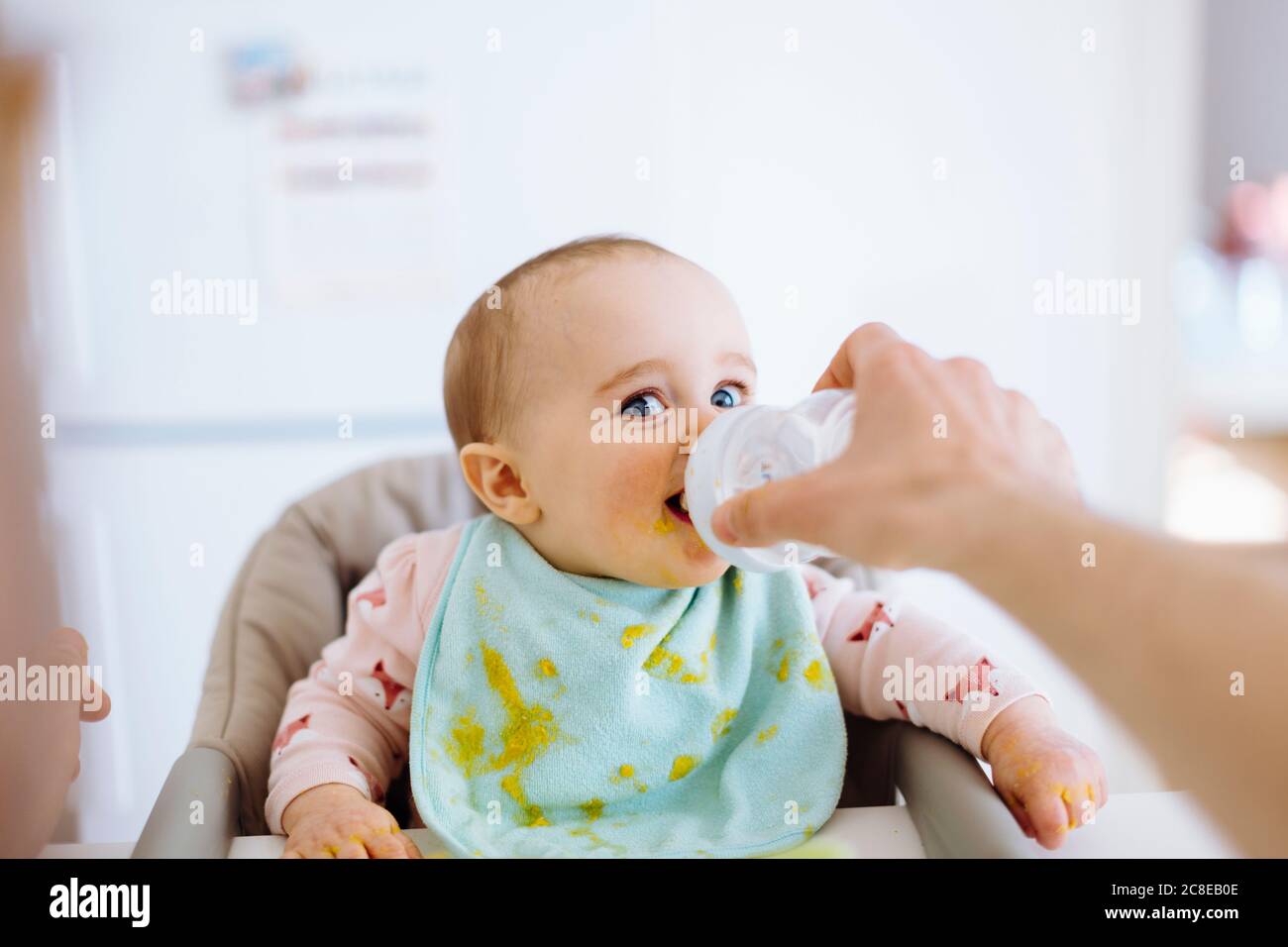 Vater hält Flasche mit Wasser für Baby Mädchen in der Höhe Stuhl Stockfoto