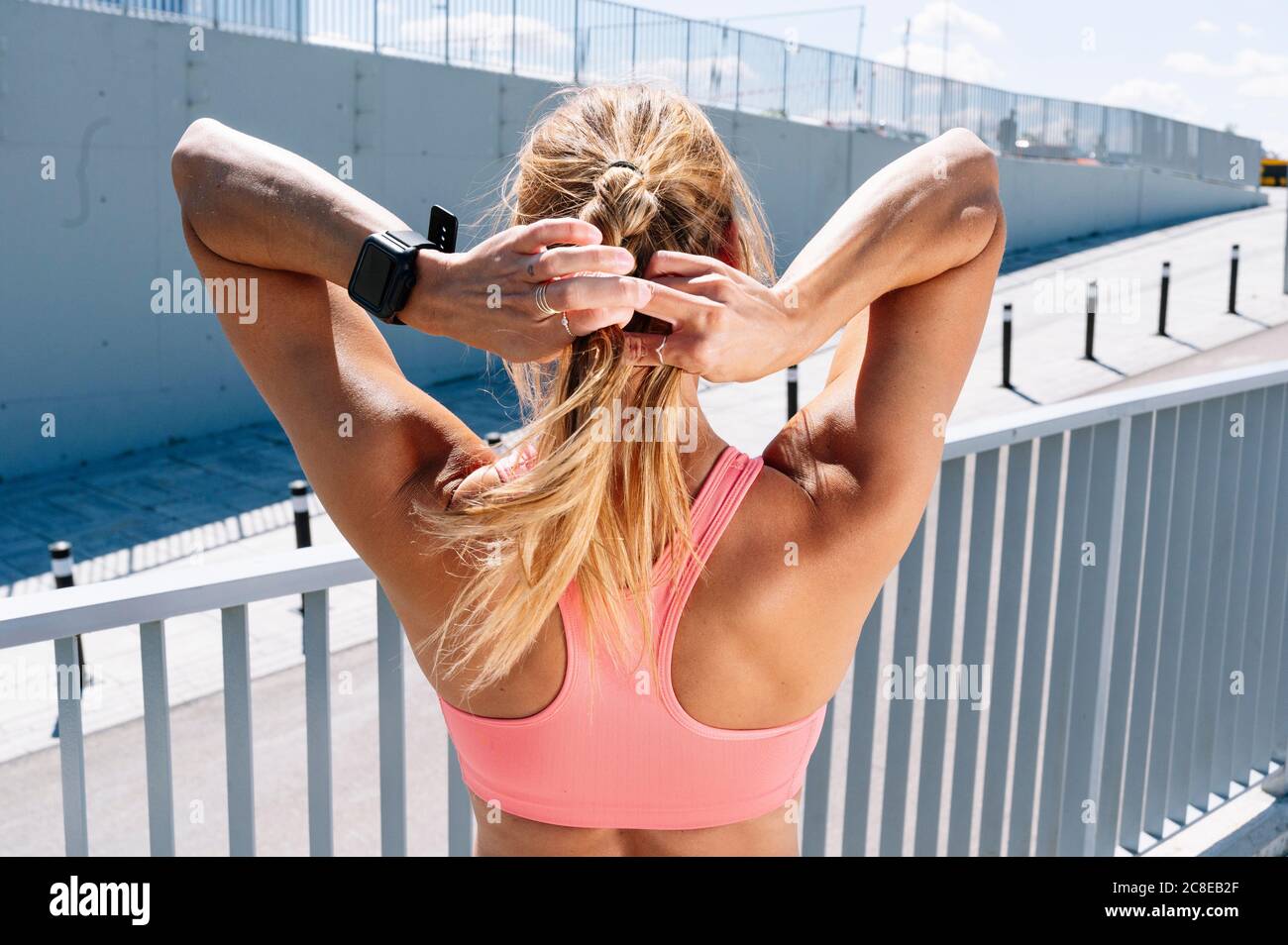 Sportliche Frau Flechten blonden Haaren während sonnigen Tag Stockfoto