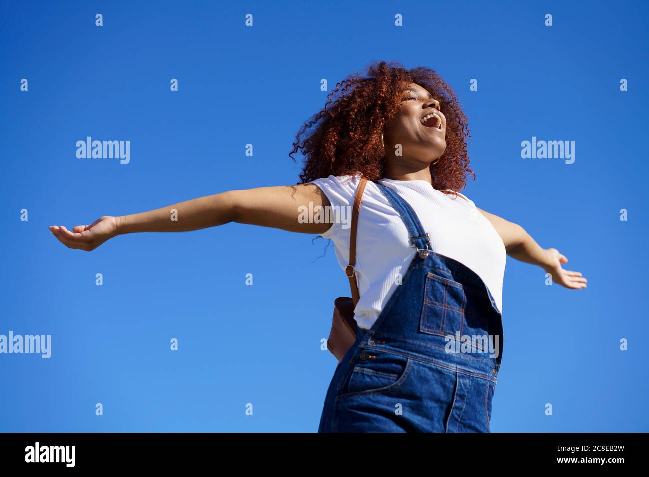 Sorglose Afro-Frau mit ausgestreckten Armen, die gegen klares Blau steht Himmel Stockfoto
