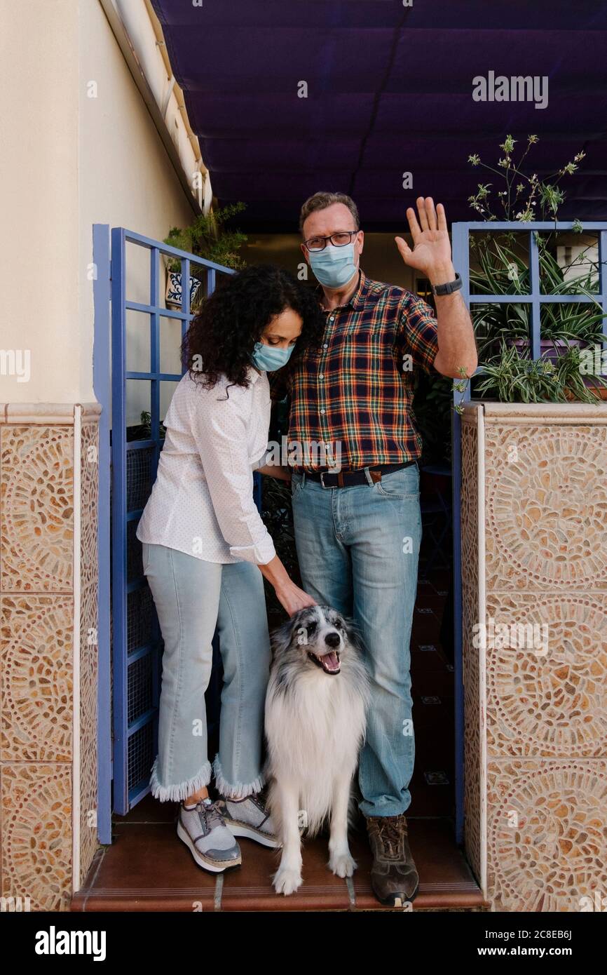 Mann mit Maske winkende Hand, während Frau Blick auf Hund Stockfoto