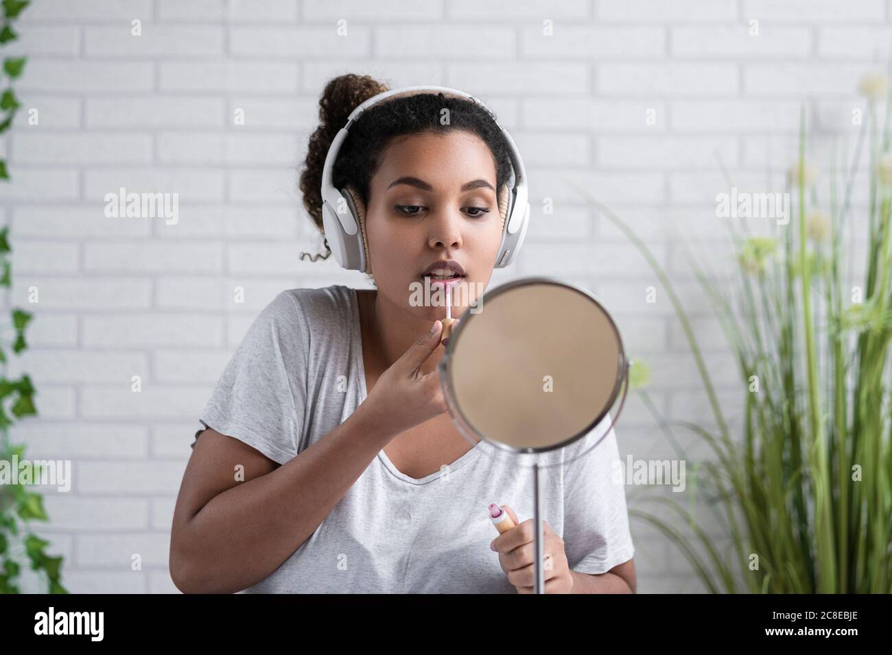 Junge Frau, die Musik über Kopfhörer mit Lipgloss auf Zu Hause Stockfoto