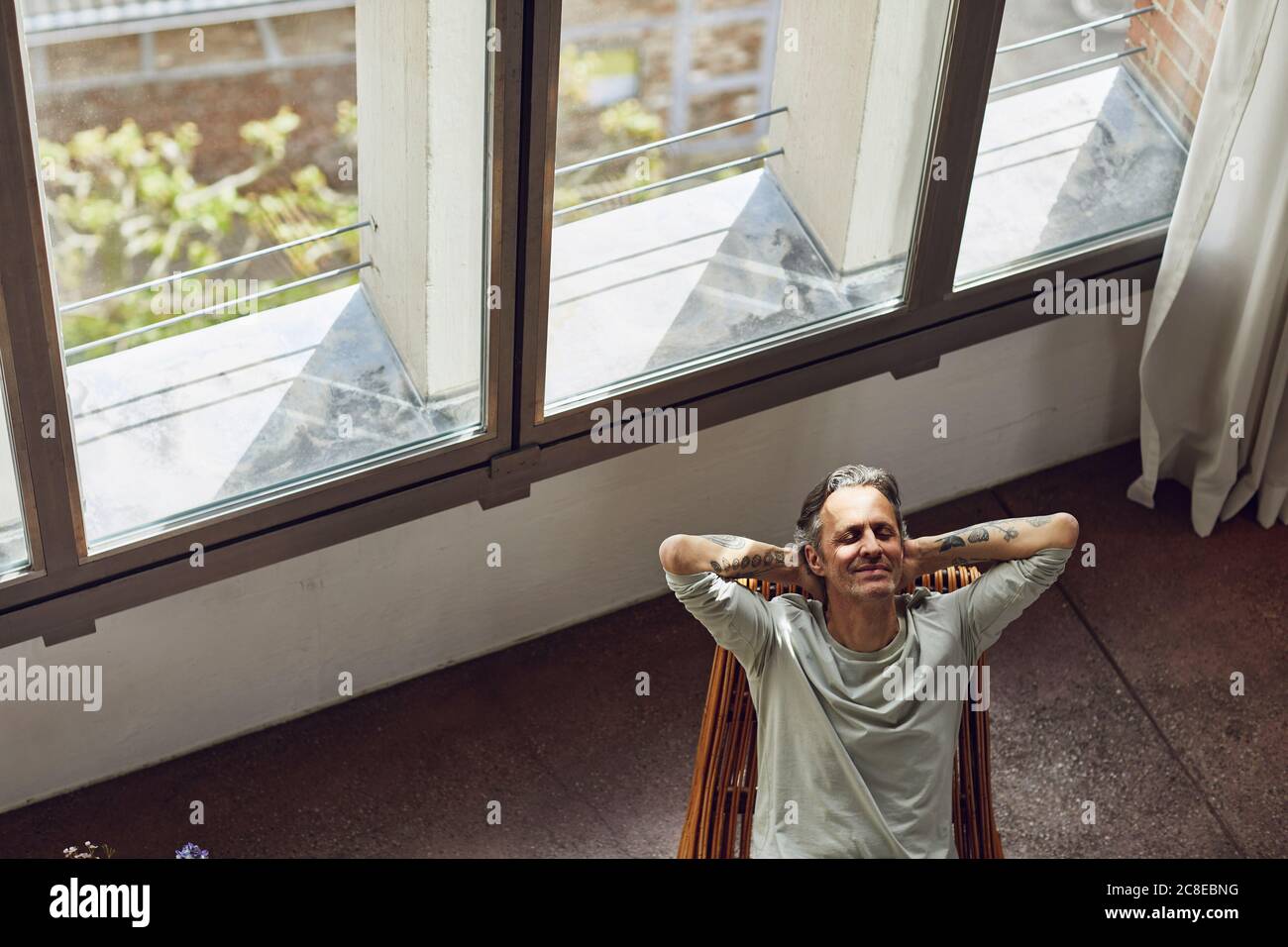 Älterer Mann, der sich auf einem Stuhl in einer Loft-Wohnung entspannt Stockfoto