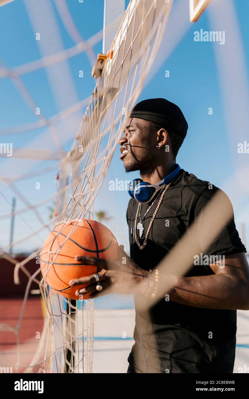 Junger Mann hält Basketball wegschauen, während beim Netz stehen Vor Gericht Stockfoto