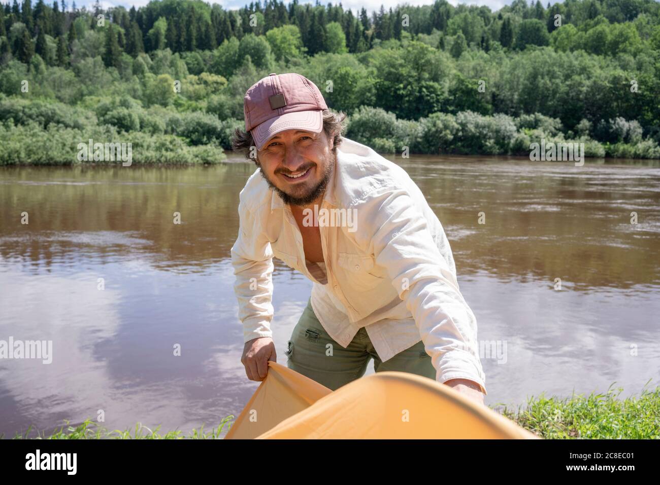 Lächelnder, mittelerwachsener Mann, der Zelt aufstellend, während er gegen See stand Im Wald Stockfoto
