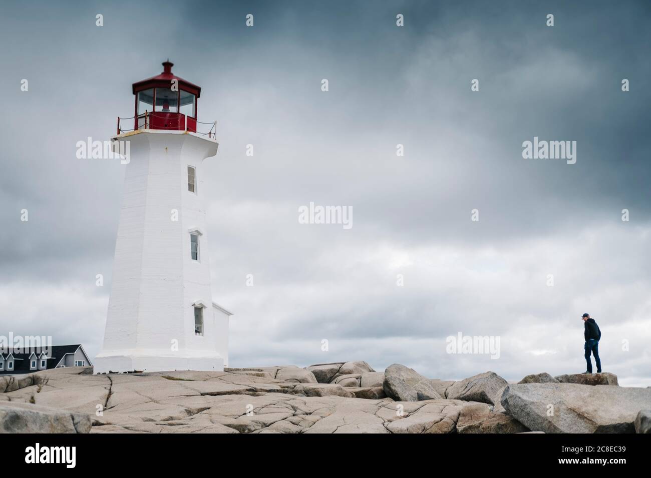 Mann, der in der Nähe von Peggys Point Lighthouse auf Felsformation gegen bewölkten Himmel steht, Nova Scotia, Kanada Stockfoto
