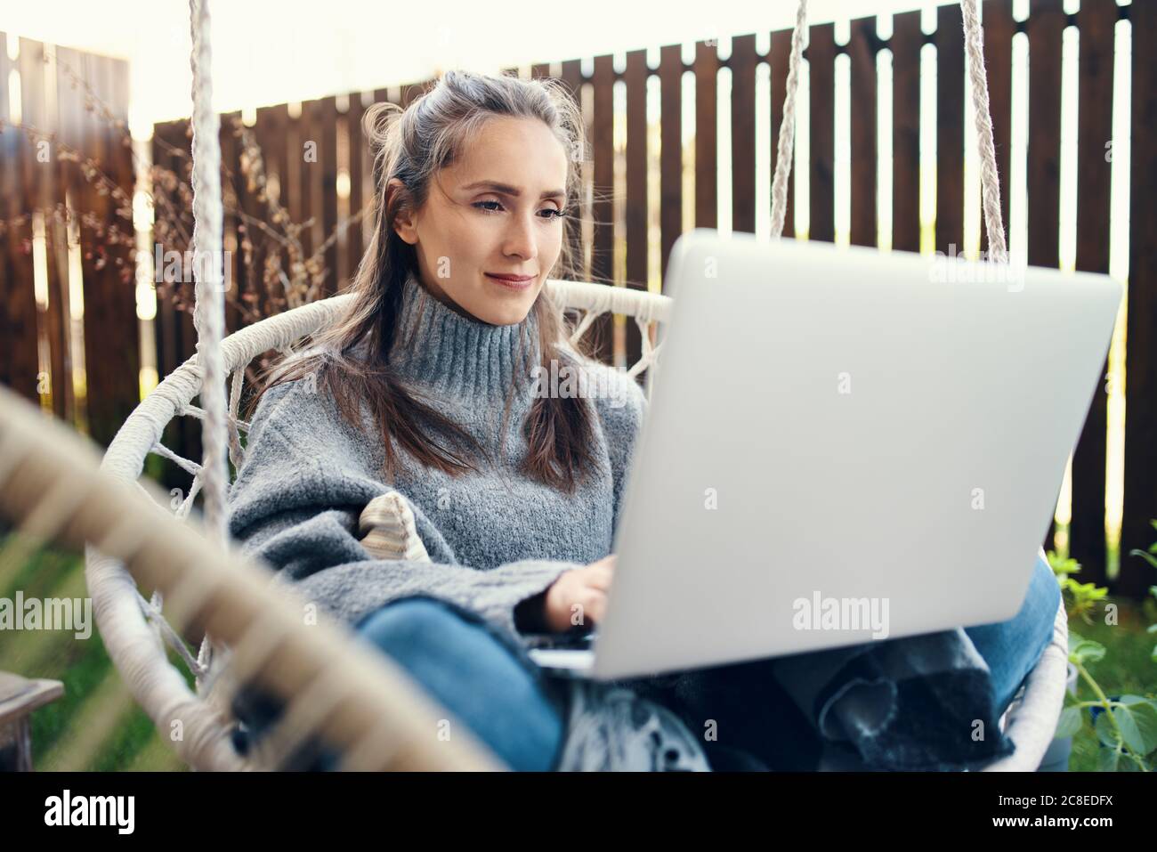 Schöne junge Frau mit Laptop, während auf Schaukel in sitzen Garten Stockfoto