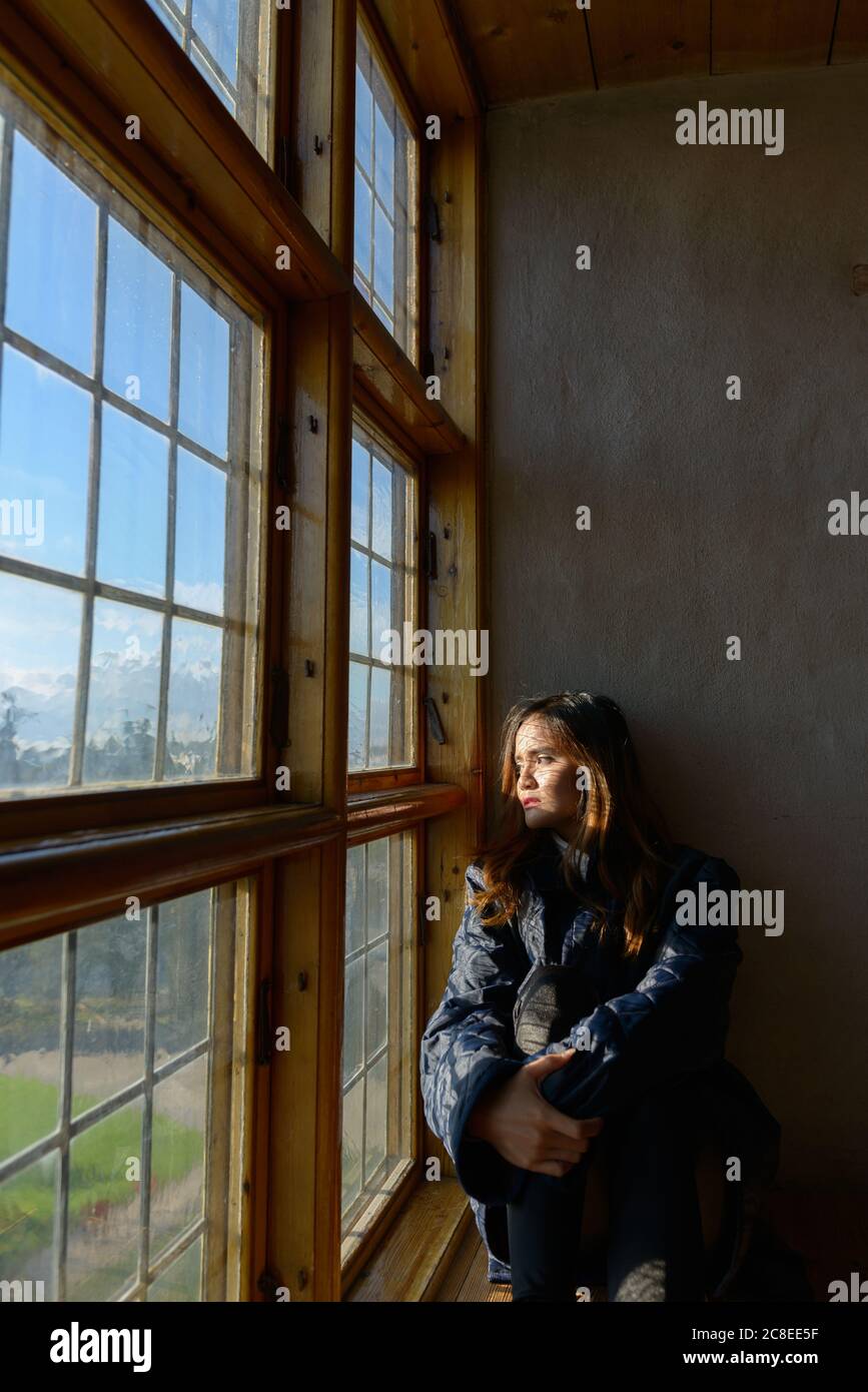 Junge schöne asiatische Frau vor geschlossenen Holzfenster mit Sonnenlicht ins Zimmer Stockfoto