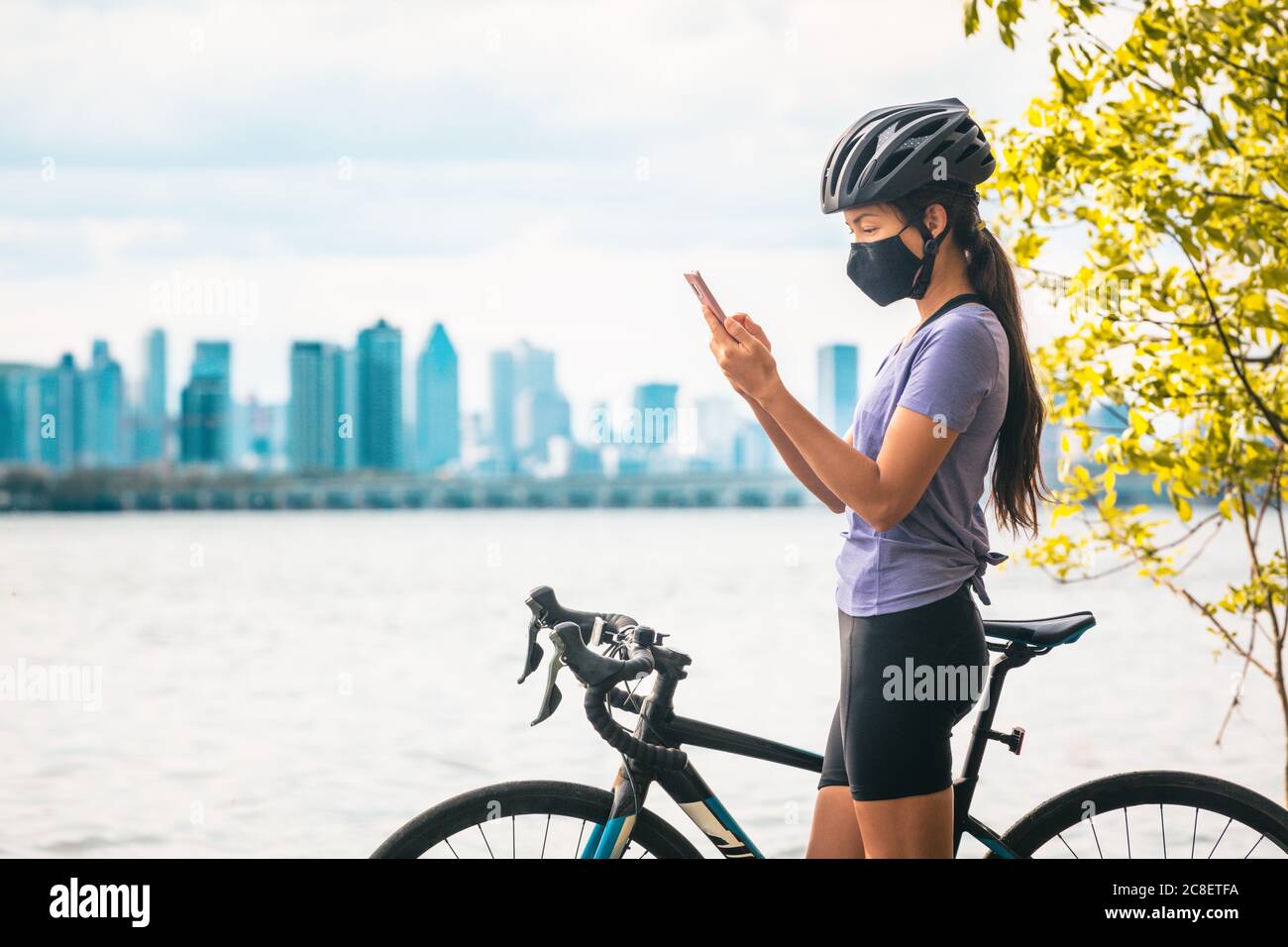 Fahrradfahrer mit Handy für Kontakt Tracing App trägt COVID-19 Gesichtsmaske als Coronavirus Prävention während der Fahrt mit dem Rennrad außerhalb der Stadt Stockfoto
