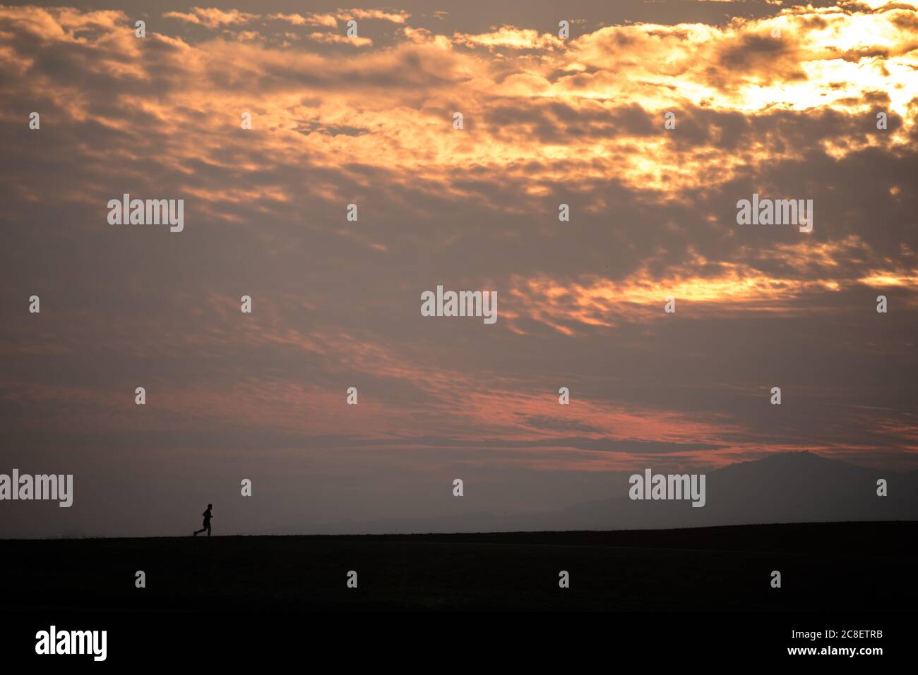 Ein Mann, der auf den Hügel mit dem dramatischen Himmel Hintergrund läuft. Stockfoto
