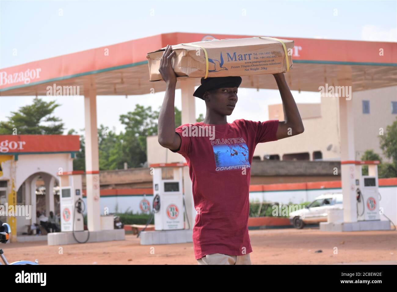 Ein junger Mann aus Afrika, der einen Karton auf dem Kopf trägt und mit den Händen seine Ladung ausbalanciert Stockfoto