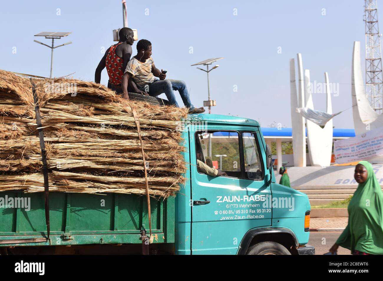 In Niamey, Niger, Afrika, sitzen zwei Arbeiter auf einem mit Strohmatten beladenen Lieferwagen. Stockfoto