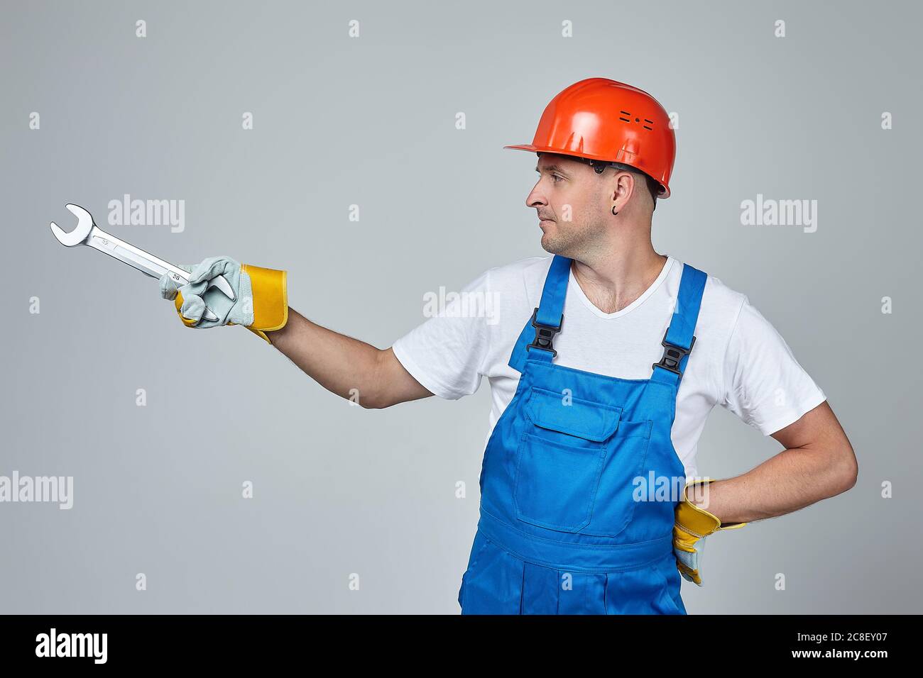 Erwachsener Mann in einem Bauhelm zeigt mit einem Schraubenschlüssel auf den Platz für den Text. Konzept der Bauleistungen Stockfoto